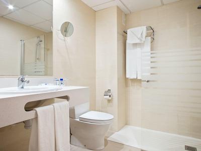 Baño de hotel luminoso con inodoro, lavabo, toallas y área de ducha con mampara de vidrio.