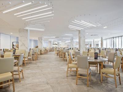 Amplio comedor moderno con muchas sillas y mesas en colores neutros y mucha luz.