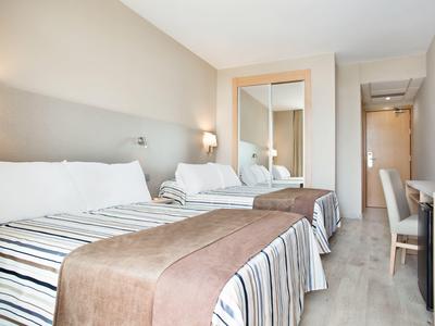 Habitación de hotel luminosa con dos camas individuales, un sillón y un gran espejo en el armario.