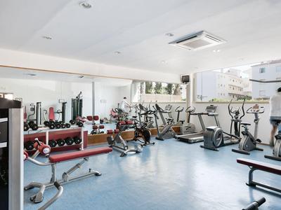 Moderner Fitnessraum mit verschiedenen Geräten und großem Spiegel.