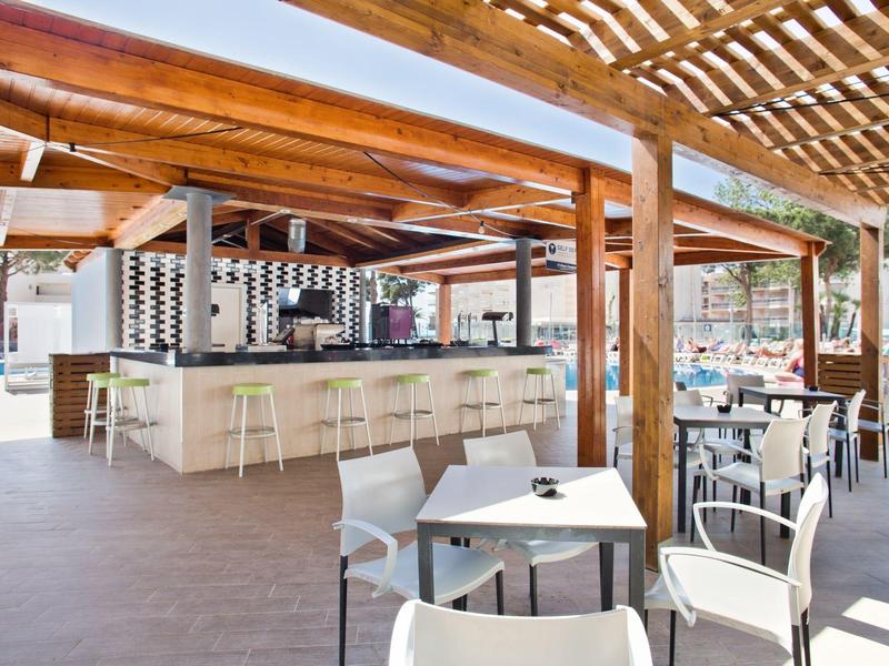 Área exterior moderna de un bar de hotel con asientos y techo de pérgola a plena luz del día.