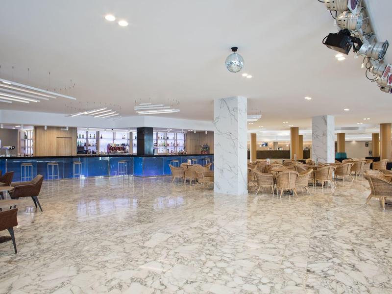 Amplio vestíbulo de hotel con suelos de mármol y áreas de descanso con sillas y mesas.