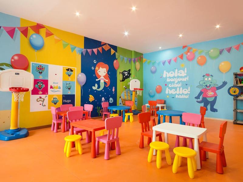 Sala de juegos colorida para niños con mesas pequeñas, sillas y aro de baloncesto en un hotel.