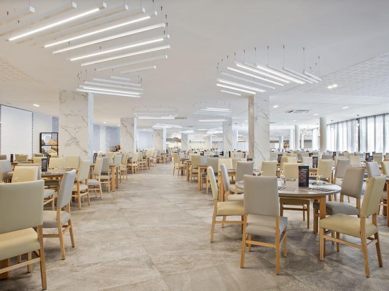 Amplio comedor moderno con muchas sillas y mesas en colores neutros y mucha luz.