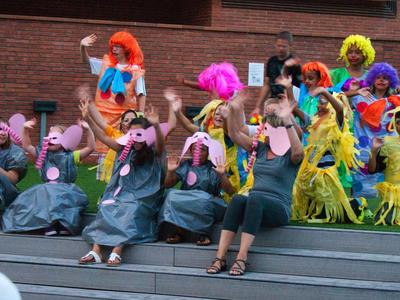 Kinder und Erwachsene in bunten Kostümen und Tiermasken sitzen auf Stufen vor einer Wand.