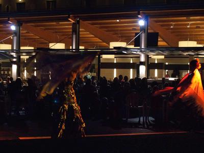 Due ballerini con tessuti colorati davanti a un pubblico illuminato all'aperto.