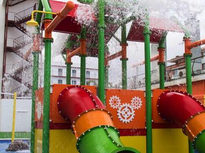Buntes Wasserspiel mit Rutschen und Spritzdüsen auf blauer Bodenfläche vor Gebäuden.