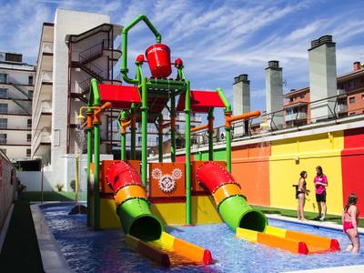 Buntes Wasserspiel mit Rutschen und Eimern, umgeben von urbanen Gebäuden und blauem Himmel.
