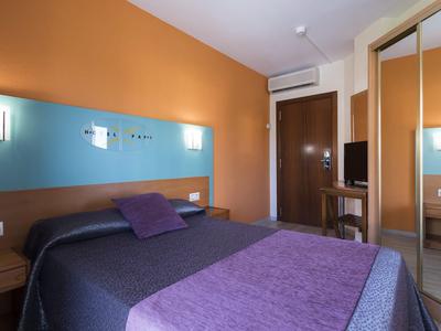 Modern hotel room with double bed, blue and orange walls, and mirrored wardrobe