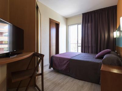 Modern hotel room with double bed, desk, chair, and window with curtains.