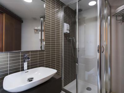 Modern bathroom with glass shower, sink, and gray tiles on the wall.
