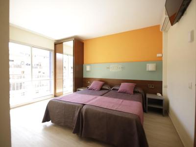 Hotel room with two single beds, purple bedding, orange wall, and balcony view in daylight