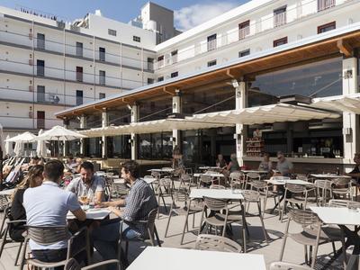 Outdoor seating area of a hotel with many tables and few guests in sunny weather