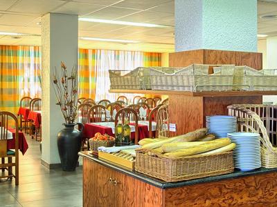 Restaurant mit Holzmöbeln, bunten Vorhängen und Buffetbereich mit Obst und Geschirr.