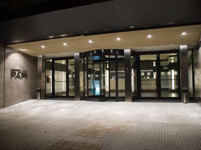 Modern beleuchteter Eingangsbereich mit Glastüren und Betonwänden, ruhige Atmosphäre nachts.