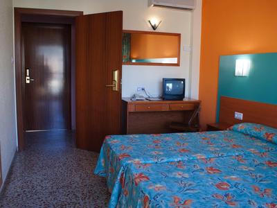 Kleines Hotelzimmer mit zwei Betten, buntem Bettbezug, einem Schreibtisch mit Fernseher und oranger Wand.