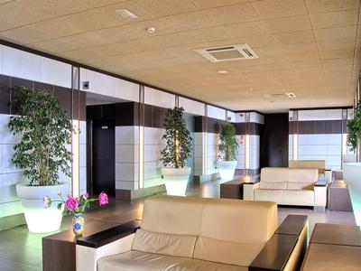 Moderne Lounge mit beigen Sofas, großen Pflanzen in beleuchteten Töpfen und Holzdecke.