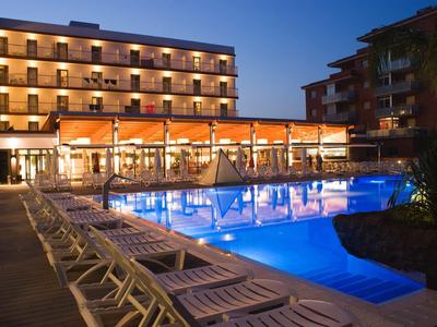 Beleuchtetes Hotel mit beleuchtetem Außenpool und Reihen von Liegestühlen am Abend.