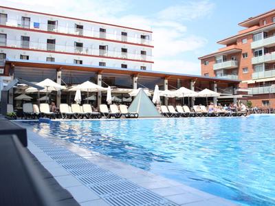 Large hotel pool with lounge chairs and umbrellas in front of multi-story buildings under clear sky