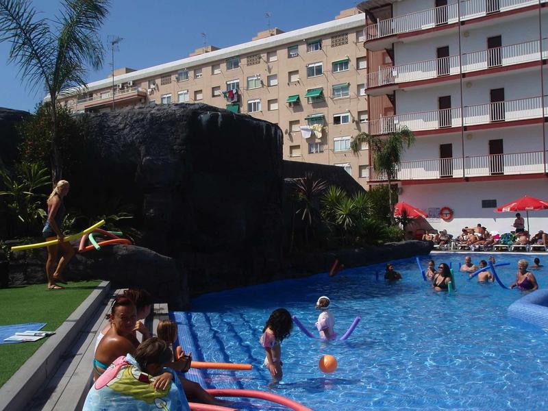 Ein großer Pool mit mehreren Schwimmern, Sonnenschirmen und Wohngebäuden im Hintergrund.