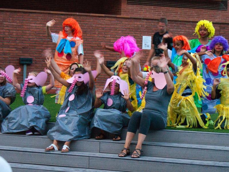 Kinder und Erwachsene in bunten Kostümen und Tiermasken sitzen auf Stufen vor einer Wand.