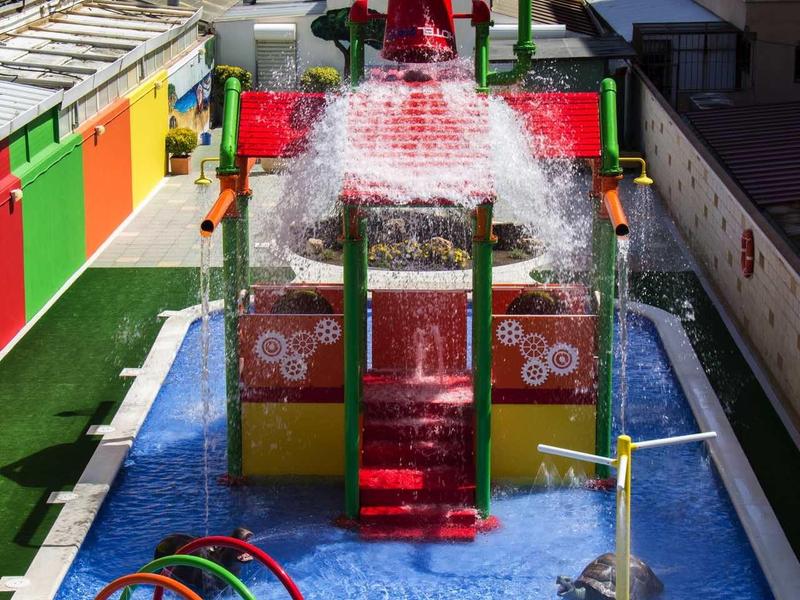 Buntes Wasserspiel mit Rutschen, Spritzringen und Figuren in flachem Becken im Außenbereich.