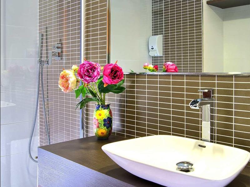 Modernes Badezimmer mit weißem Waschbecken, braunen Fliesen und buntem Blumenstrauß auf der Theke.