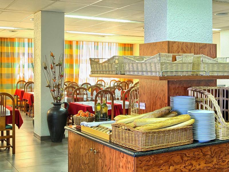 Restaurant mit Holzmöbeln, bunten Vorhängen und Buffetbereich mit Obst und Geschirr.