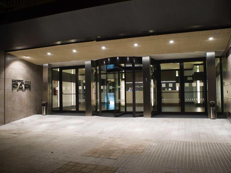 Modern beleuchteter Eingangsbereich mit Glastüren und Betonwänden, ruhige Atmosphäre nachts.