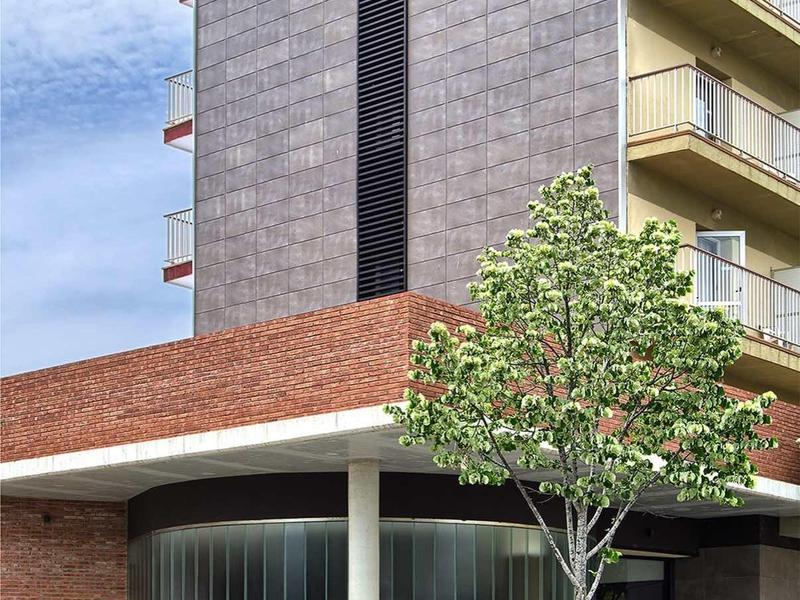 Modernes Hotelgebäude mit dunklen Fassaden, Balkonreihen und Baum vor Glasfront und Eingang.