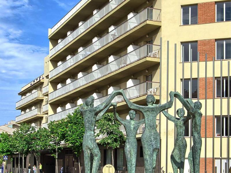 Moderne Bronze-Skulpturen vor einem mehrstöckigen gelblichen Gebäude unter blauem Himmel.