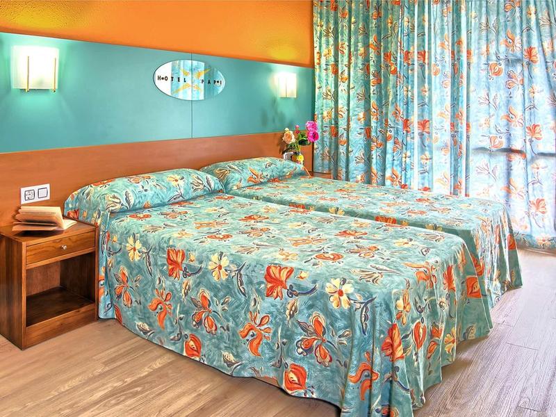 Gemütliches Schlafzimmer mit Doppelbett, buntem Blumenbettbezug, Holzmöbeln und blauen Vorhängen.