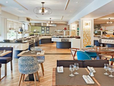 Großer, heller Restaurantraum mit verschiedenen Sitzgelegenheiten, Holzboden und modernem Licht.