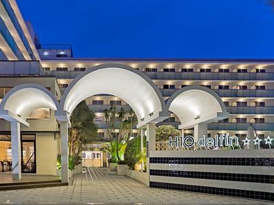 Modernes Hotel mit beleuchteten weißen Bögen und mehreren Stockwerken bei Abenddämmerung.