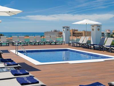 Moderner Poolbereich mit Sonnenliegen, Sonnenschirmen und Blick aufs Meer an einem sonnigen Tag.