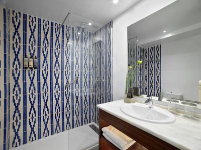 Moderne Badezimmerecke mit blau-weiß gemusterter Wand, Dusche und Waschbecken mit Marmorplatte.