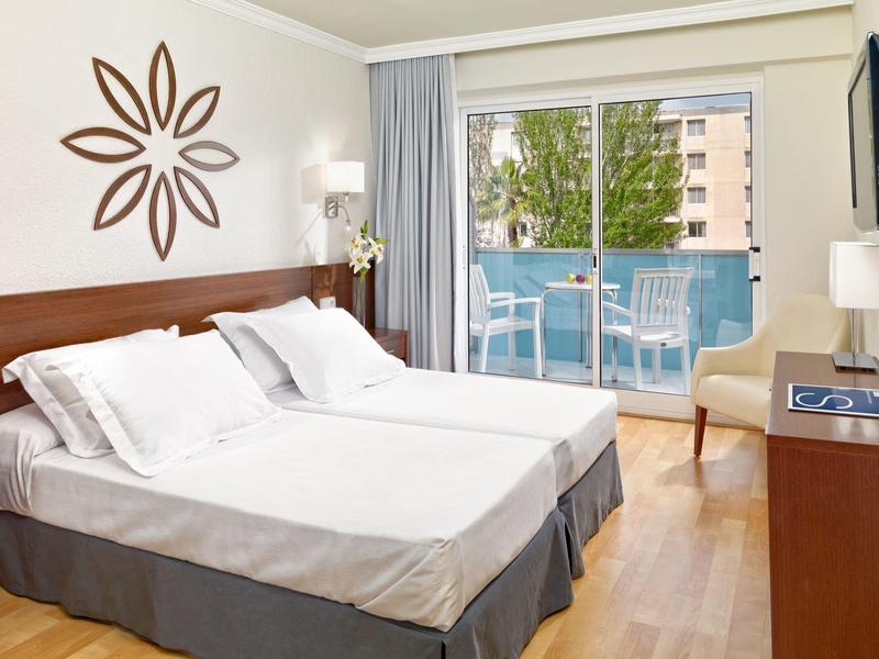 Helles Hotelzimmer mit Doppelbett, Holzmöbeln, Balkon und moderner Wanddekoration.