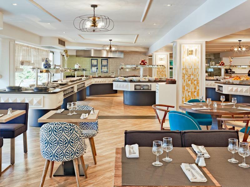 Großer, heller Restaurantraum mit verschiedenen Sitzgelegenheiten, Holzboden und modernem Licht.