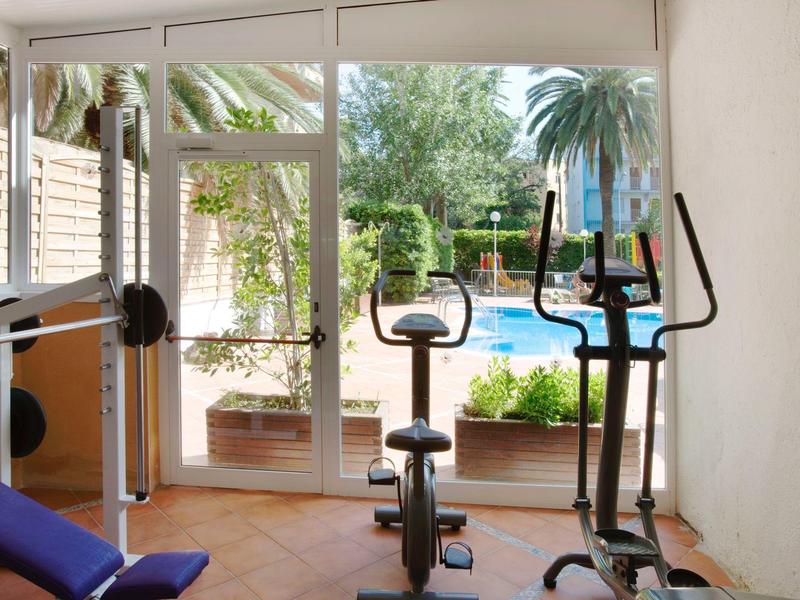 Kleines Fitnesszimmer mit zwei Geräten, Hantelbank, großem Fenster und Blick auf Terrasse mit Pflanzen.