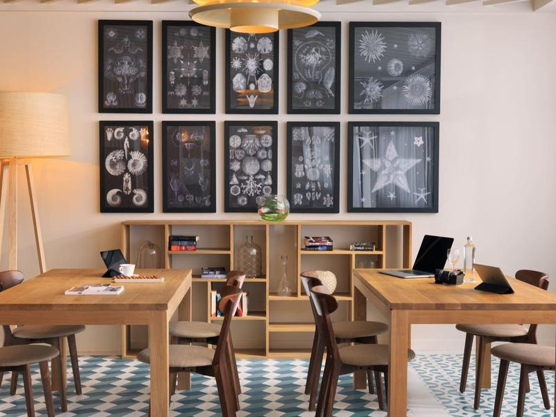 Nowoczesna jadalnia z drewnianymi stołami, krzesłami, lampą podłogową i oprawionymi nadrukami botanicznymi.