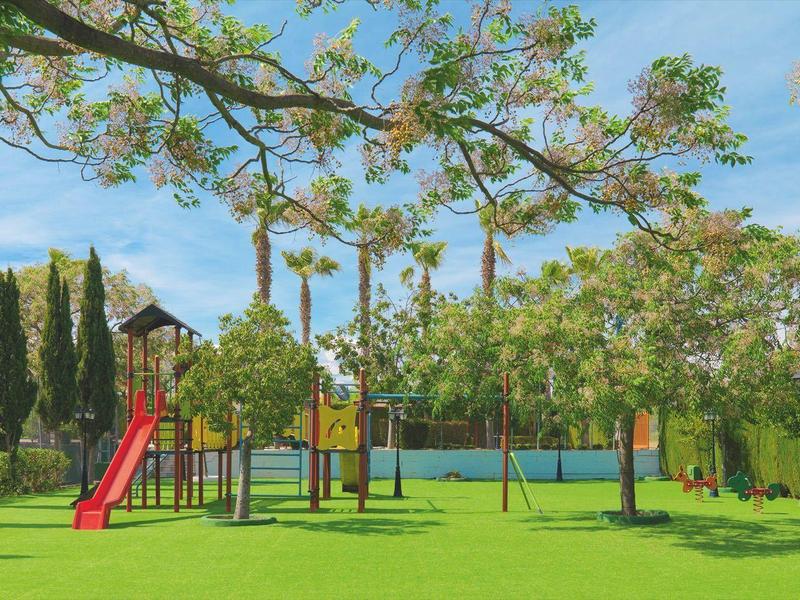 Plac zabaw ze zjeżdżalniami i konstrukcjami do wspinaczki w zielonym parku pod częściowo zachmurzonym niebem.