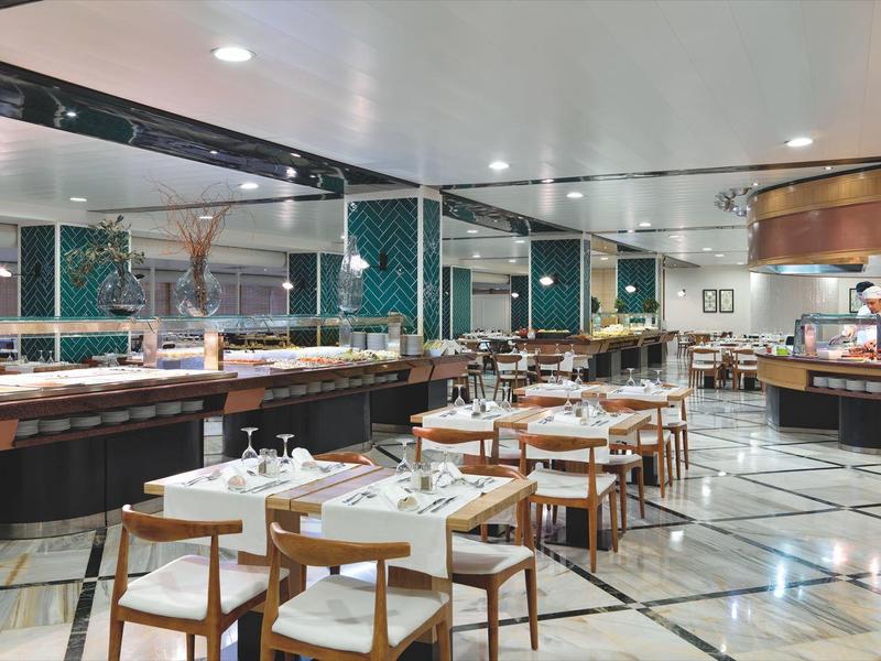 Przestronna nowoczesna restauracja hotelowa z drewnianymi krzesłami, białymi stołami i bufetem.