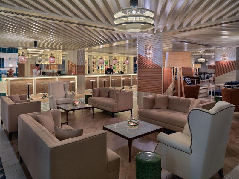 Nowoczesna lobby hotelowa z wygodnymi sofami, fotelami i stolikami pod paskowym sufitem z ciepłym oświetleniem.