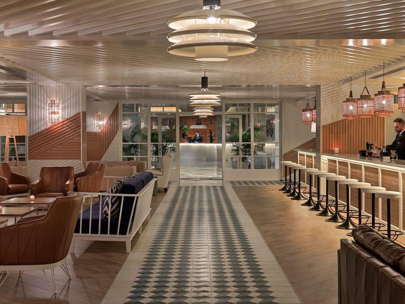 Nowoczesny hotelowy salon z skórzanymi fotelami, barem i wzorzystą podłogą.