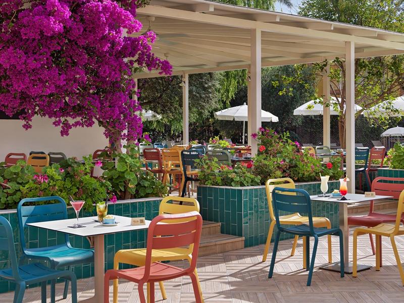 Przestrzeń na świeżym powietrzu z kolorowymi krzesłami i stołami pod patio obok różowych kwiatów.