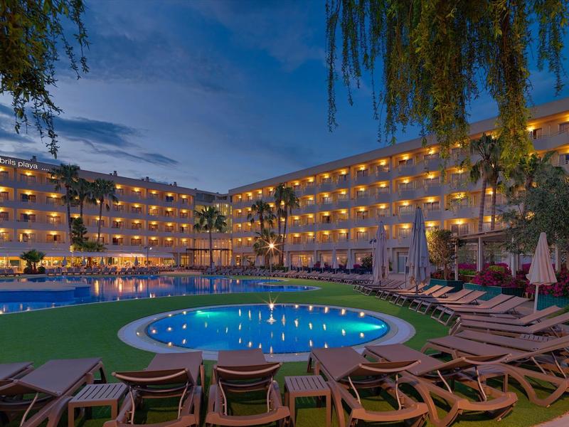 Hotel z oświetlonymi balkonami wokół basenu o zmierzchu.