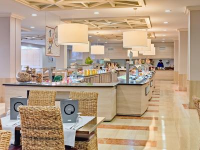 Nowoczesna strefa śniadaniowa w hotelu z bufetem, krzesła z rattanu i ciepłe oświetlenie.