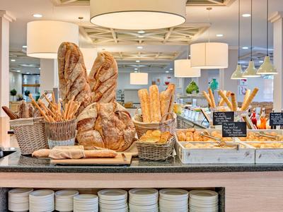 Różnorodne świeże pieczywo i bagietki ułożone w koszykach na hotelowym bufecie.