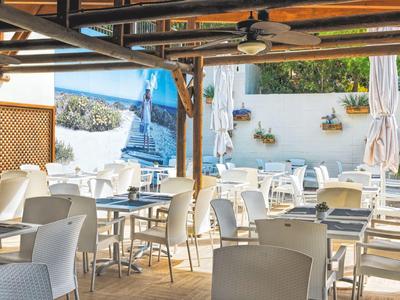 Jasny taras na zewnątrz z białymi krzesłami i stołami pod drewnianą pergolą, mural na ścianie