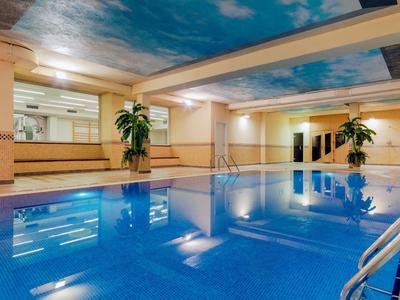 Kryty basen hotelowy z niebieską wodą, roślinami doniczkowymi i sufitem malowanym jak niebo